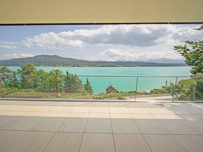 Geräumiger Balkon mit Glasgeländer und atemberaubendem Blick auf den See und die umliegende Landschaft.