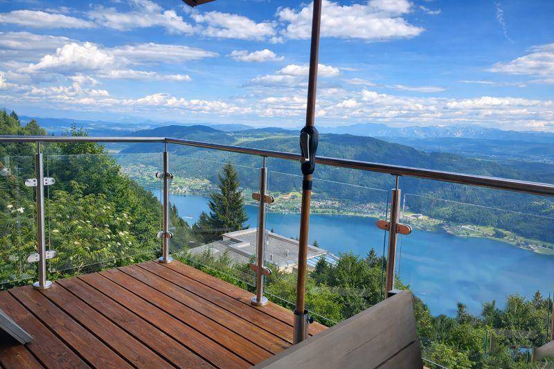 Eine Holzterrasse mit Glasgeländer und spektakulärem Blick auf einen blauen See und die umliegenden Berge.