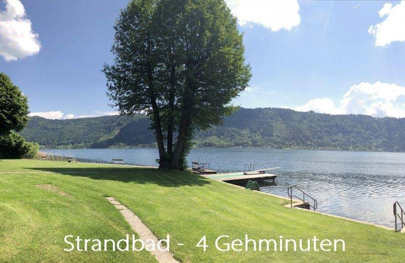 Sonniger Blick auf das Strandbad am See mit grünem Rasen und einem Steg zum Schwimmen.