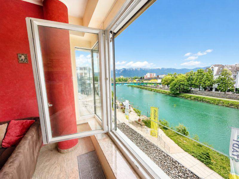 Innenraum mit roter Akzentwand und großem Fenster mit weitem Blick auf den Fluss und die Stadt.