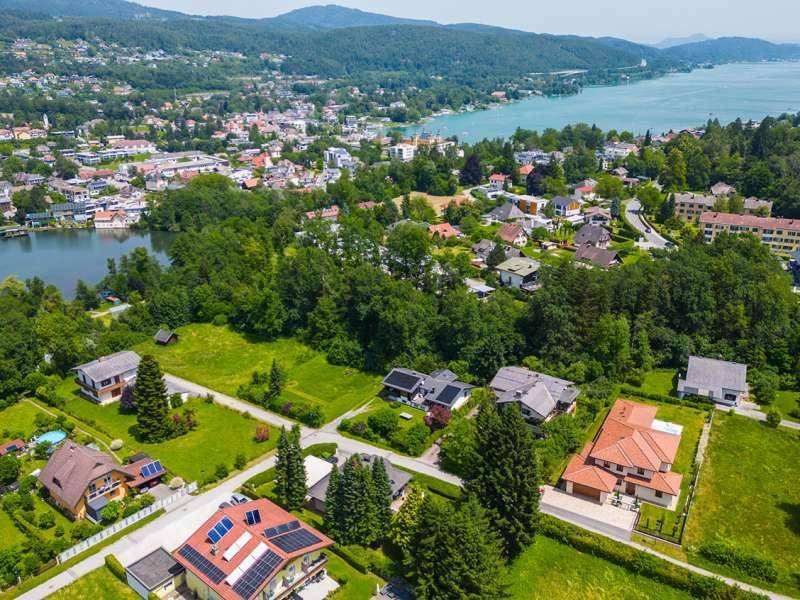 Weitläufige Luftaufnahme einer Wohnsiedlung mit vielen Grünflächen, Häusern und einem See im Hintergrund.