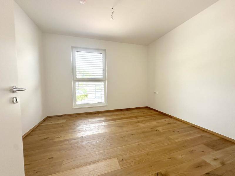 Helles Schlafzimmer mit Holzboden und einem Fenster, das viel Tageslicht hereinlässt.