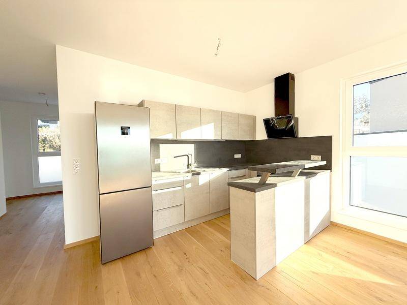 Moderne Einbauküche mit hellen Schränken, Edelstahlkühlschrank und Dunstabzugshaube.