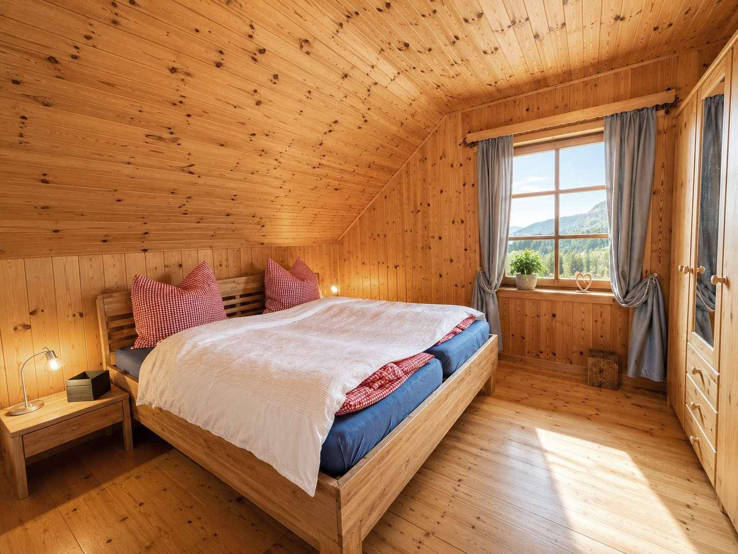 Gemütliches Schlafzimmer im Dachgeschoss mit Holzwänden, Doppelbett und Fensterblick auf die Berge.
