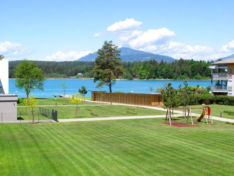 Große grüne Rasenfläche mit Kinderspielplatz und herrlichem Blick auf den See und die Berge.