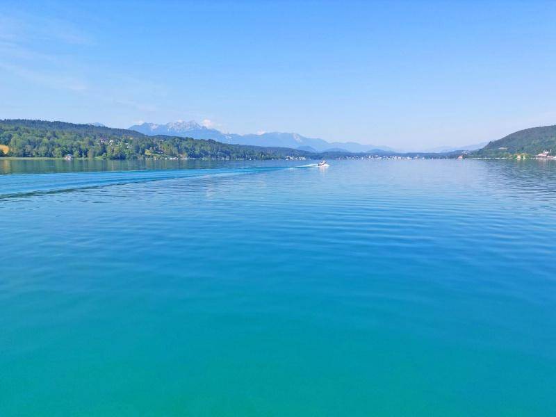 Weitläufiger Blick über den klaren See mit einem Boot und majestätischen Bergen am Horizont.