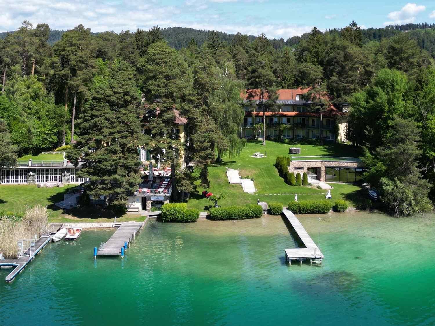 Panoramablick auf das weitläufige Anwesen am See mit privaten Stegen, Pool und üppiger Vegetation.