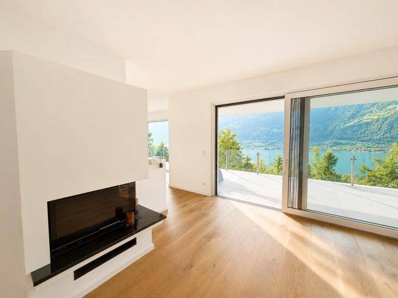 Helles Wohnzimmer mit Holzboden, modernem Kamin und großen Schiebetüren zum See.