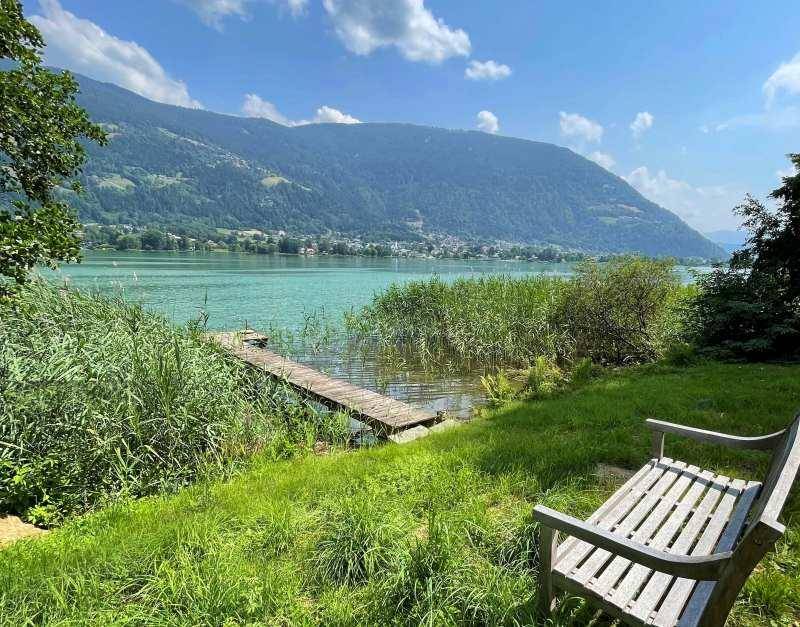 Idyllischer Blick auf den See und die umliegenden Berge von einer Holzbank aus.