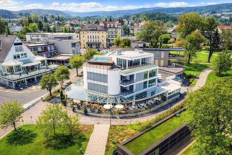 Luftaufnahme eines modernen Gebäudekomplexes mit Dachpool und umliegender Grünfläche.