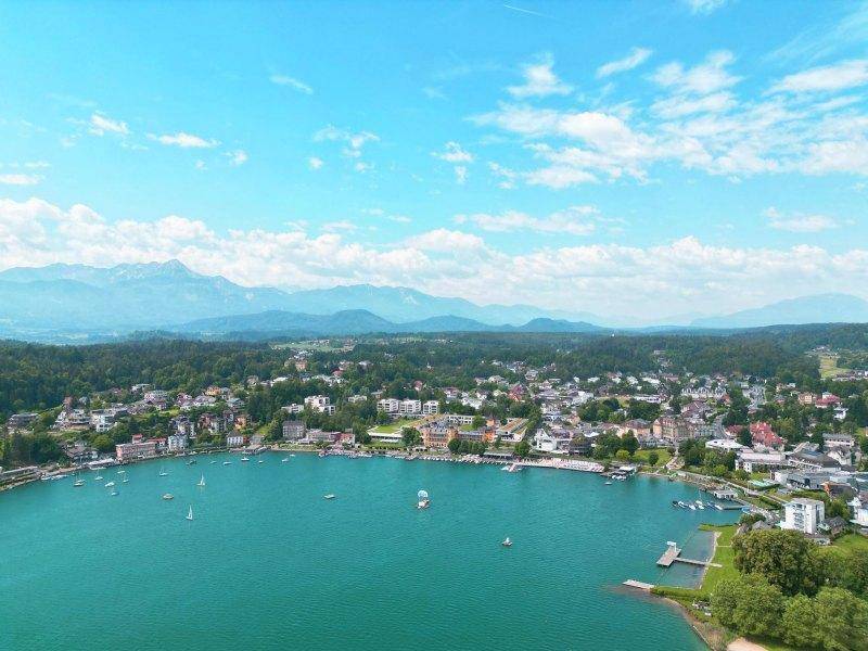 Breiter Panoramablick auf einen großen See mit Segelbooten, umgeben von einer malerischen Stadt und Bergen.