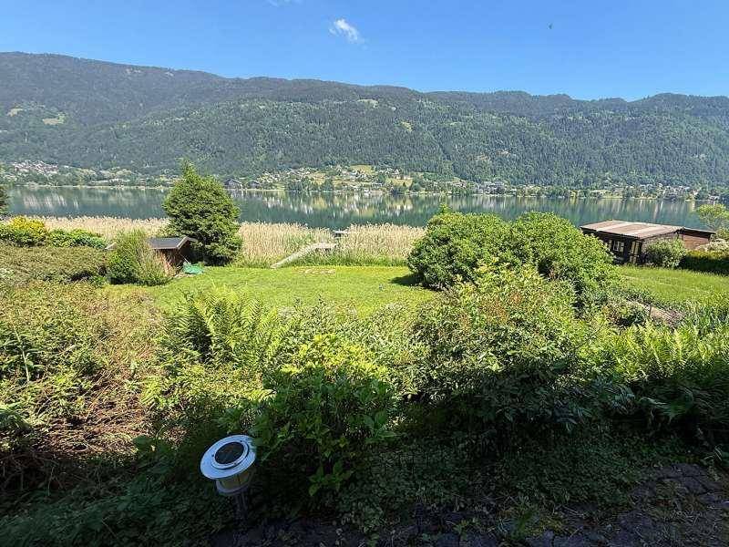 Großer Garten mit Rasenfläche und Büschen, bietet einen weiten Blick auf den See und die Berge.