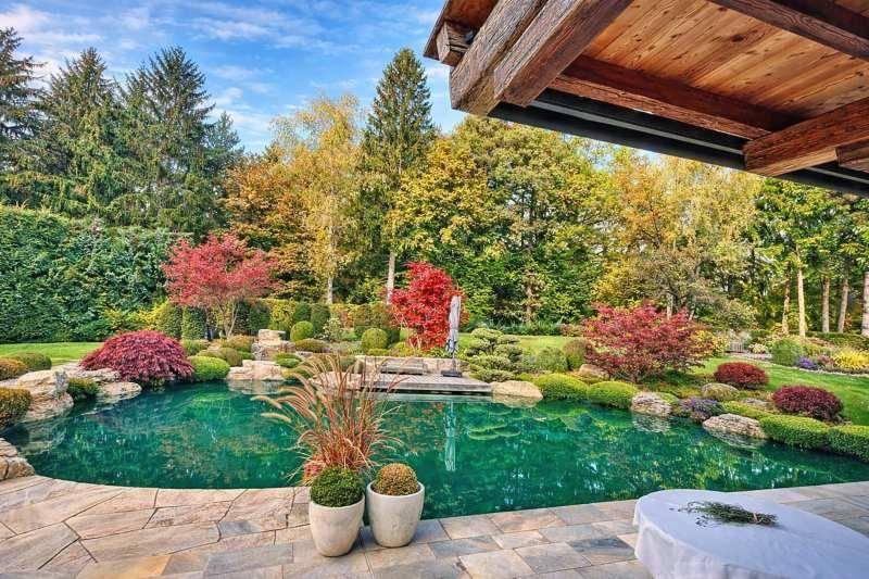Gemütliche Terrasse mit Steinboden und Blick auf den Naturpool, umgeben von herbstlicher Gartenpracht.