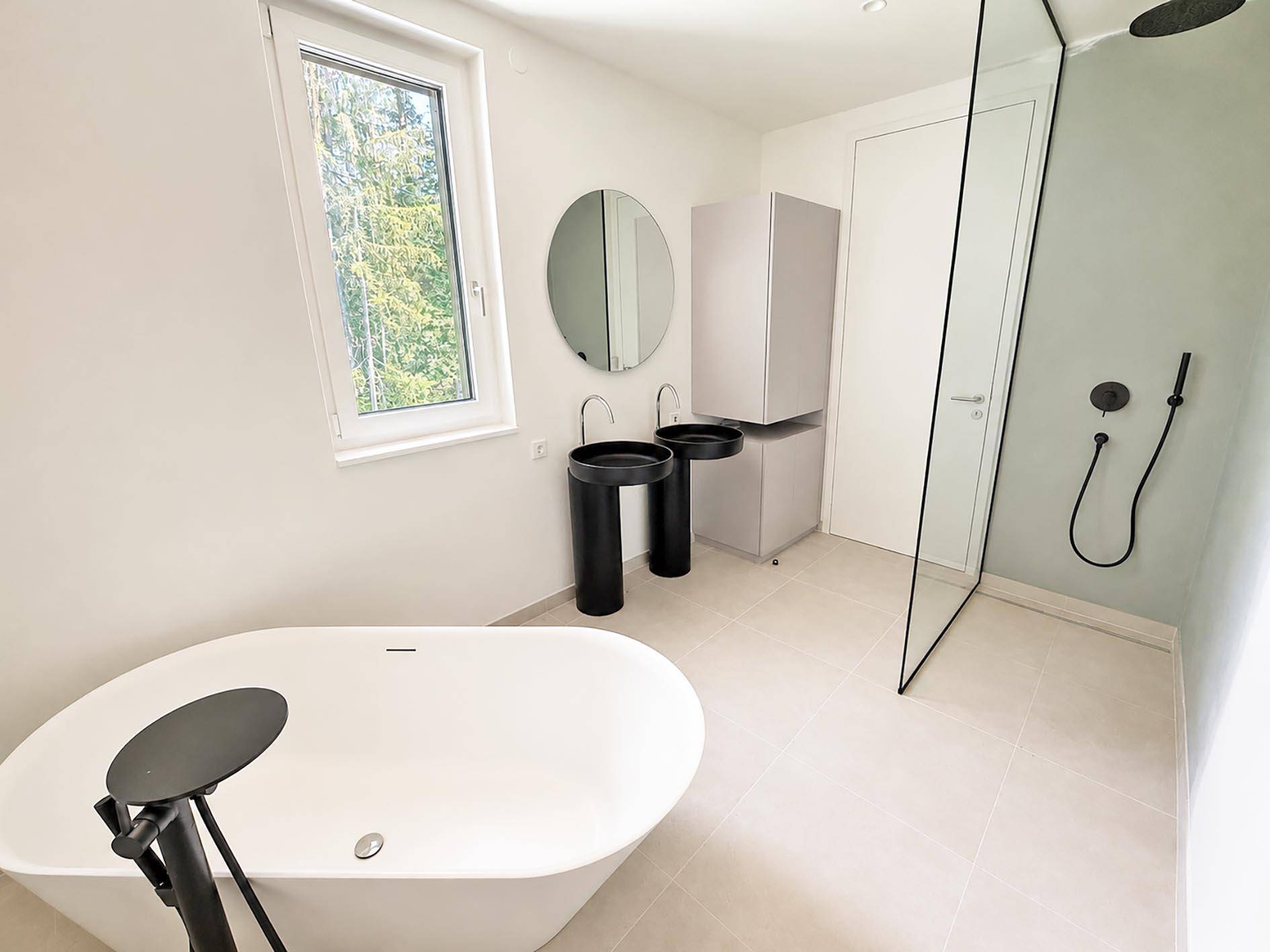 Modernes Badezimmer mit freistehender Badewanne, zwei schwarzen Waschbecken und begehbarer Dusche.