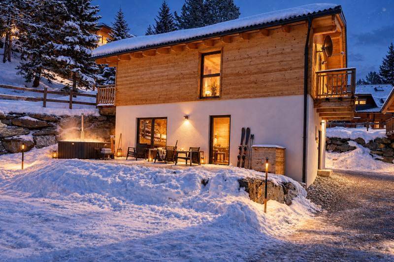 Chalet-Terrasse mit Whirlpool und Sitzgelegenheiten im Schnee, umgeben von winterlicher Berglandschaft.