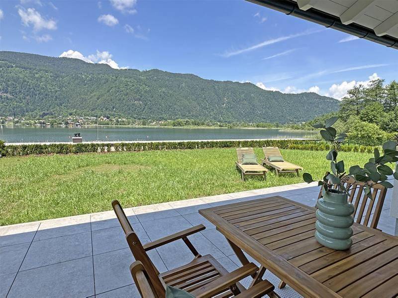 Gemütliche Terrasse mit Holztisch und Stühlen, die einen idyllischen Seeblick bietet.