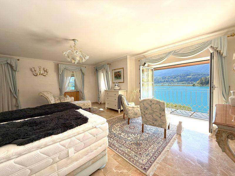Helles Schlafzimmer mit großem Bett, eleganten Vorhängen und direktem Zugang zum Balkon mit Seeblick.