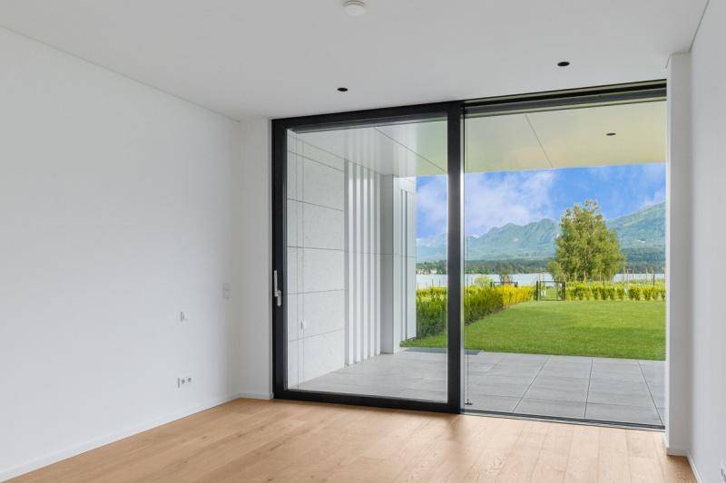 Heller, leerer Raum mit großen Glasschiebetüren und Zugang zu einer Terrasse mit Seeblick.