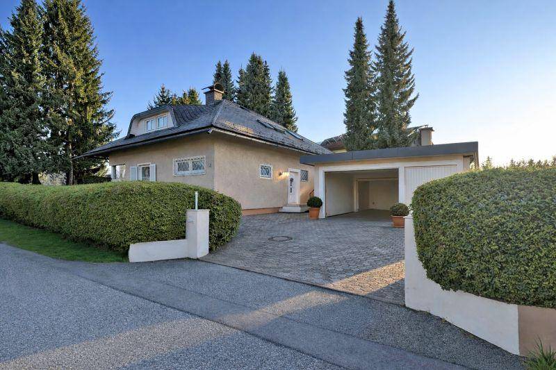 Haus mit gepflasterter Auffahrt, Garage und grüner Hecke am Straßenrand.