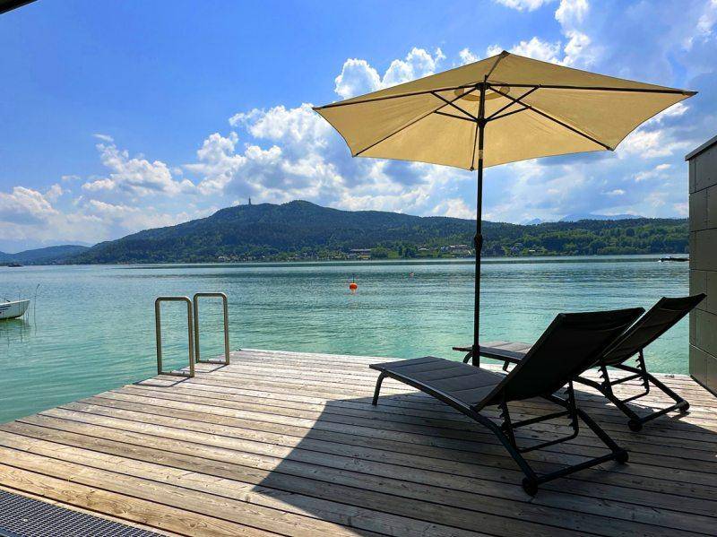 Gemütliche Holzterrasse direkt am See mit Sonnenliegen und Sonnenschirm für entspannte Stunden am Wasser.