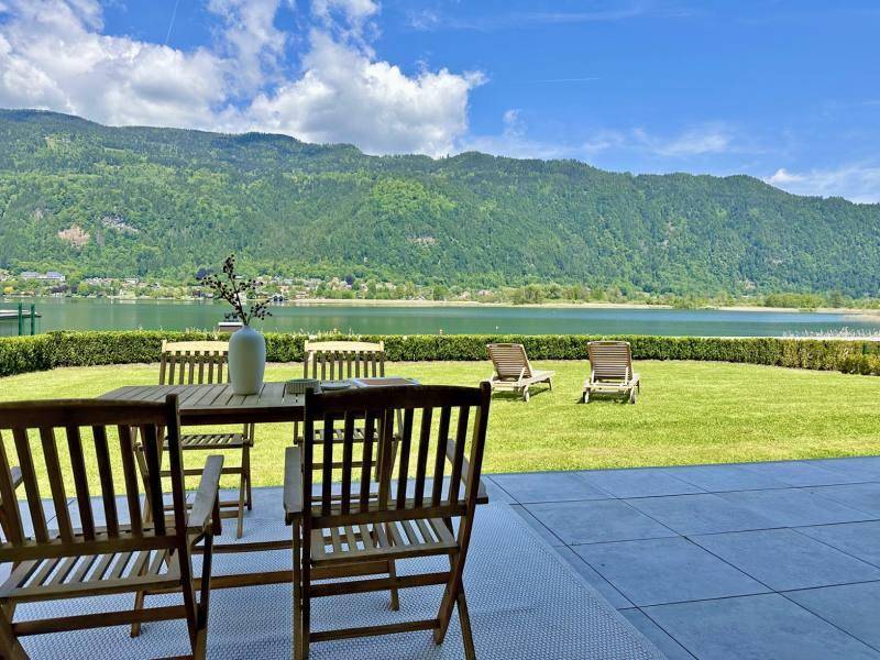 Terrasse mit Holztisch und Stühlen bietet einen weiten Blick auf den See und die Berge.