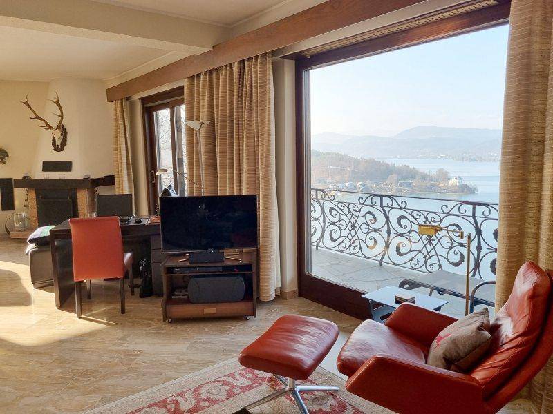 Helles Wohnzimmer mit bequemen Sesseln, Fernseher und Panoramablick auf den See.