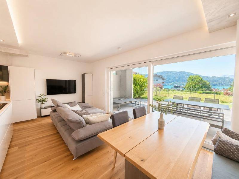 Heller Wohn-Essbereich mit Holzboden, großem Sofa und Schiebetüren zur Terrasse mit Seeblick.