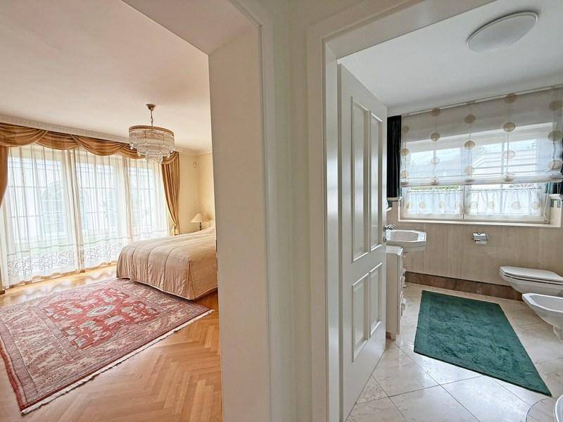 Badezimmer mit Fliesenboden, Fenster, Toilette und Bidet, angrenzend an ein Schlafzimmer.