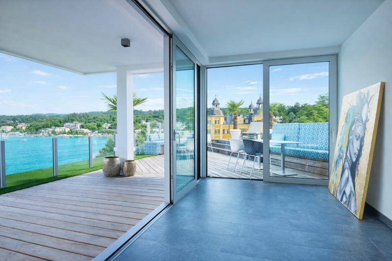 Heller Innenraum mit großen Schiebetüren, die zu einer Terrasse mit Seeblick führen.