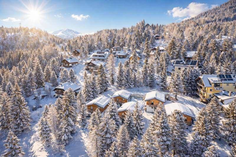 Winterliche Ansicht eines Chalet-Dorfes in einer tief verschneiten Bergregion mit vielen Bäumen.