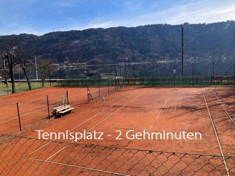 Roter Sand-Tennisplatz in der Nähe des Sees, umgeben von Bergen und Natur.
