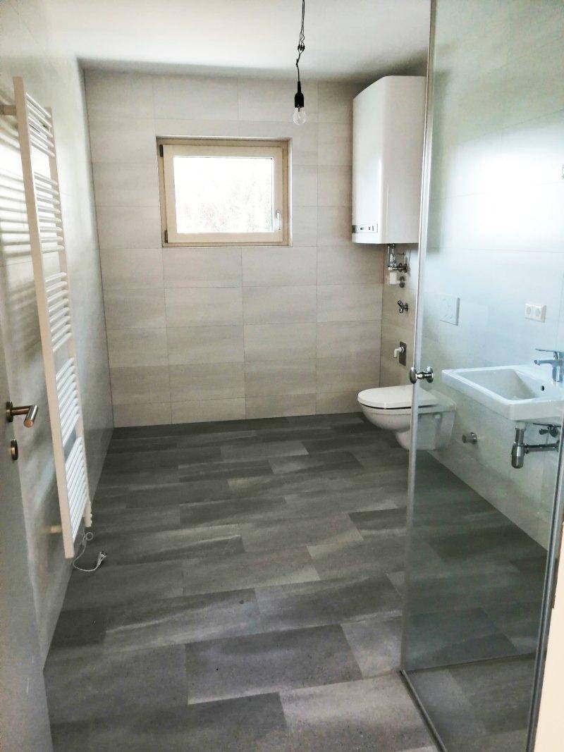 Modernes Badezimmer mit hellen Fliesen, Dusche und Fenster, ausgestattet mit einem Handtuchheizkörper.