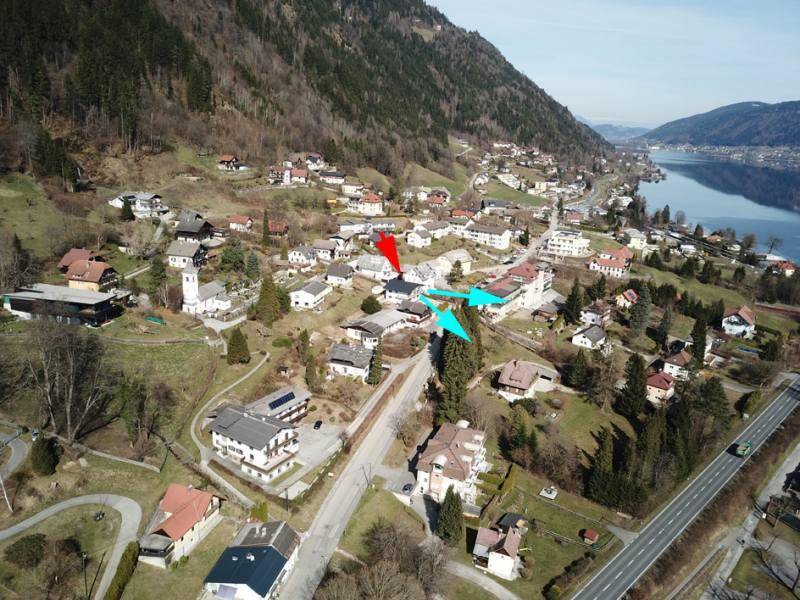 Luftaufnahme des Dorfes mit Häusern und Straßen, eingebettet in eine bergige Landschaft am See.