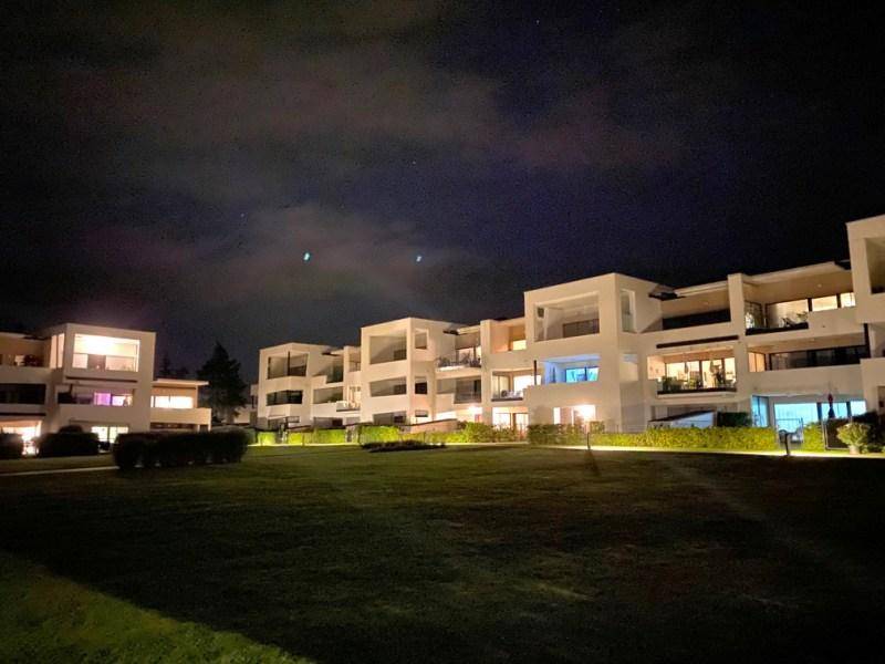 Moderne Wohngebäude bei Nacht, beleuchtet und umgeben von gepflegten Rasenflächen.