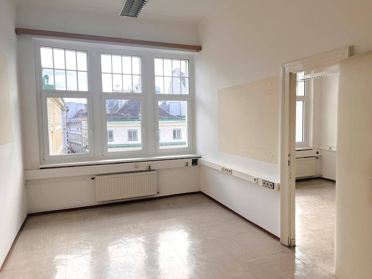 Geräumiges, leeres Büro mit hellem Boden, großen Fenstern und Blick auf die umliegenden Gebäude.