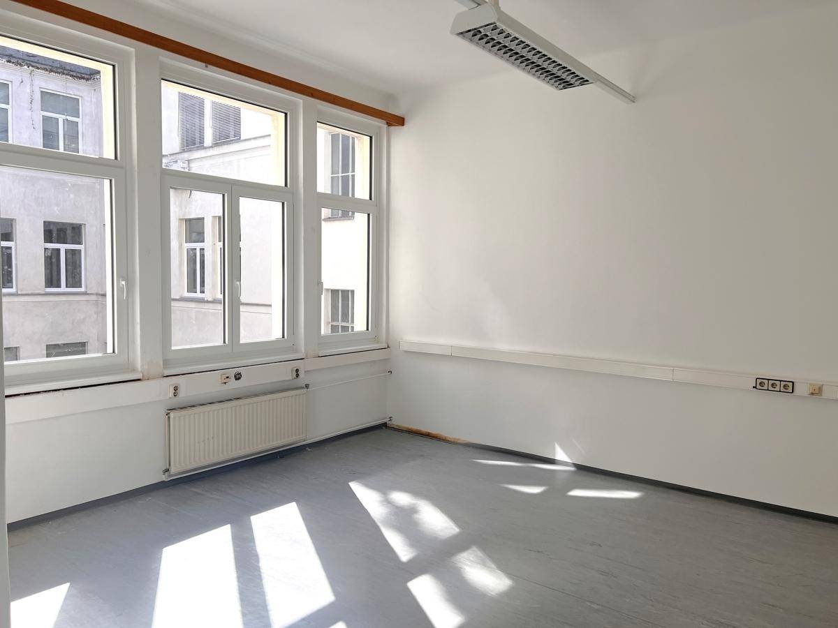 Helles Büro mit grauem Boden, weißen Wänden und großen Fenstern, durch die Sonnenlicht einfällt.