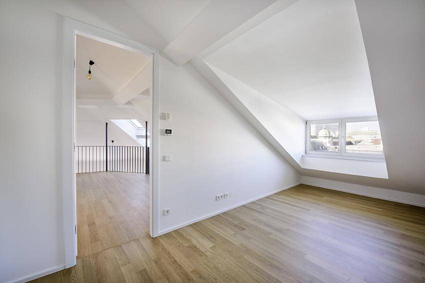 Gemütliches Dachzimmer mit schräger Decke und Fenster mit Stadtblick.