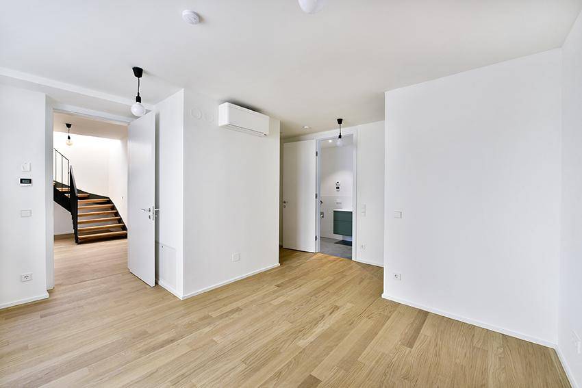 Heller Wohnbereich mit Holzboden, Klimaanlage und Zugang zur Treppe.