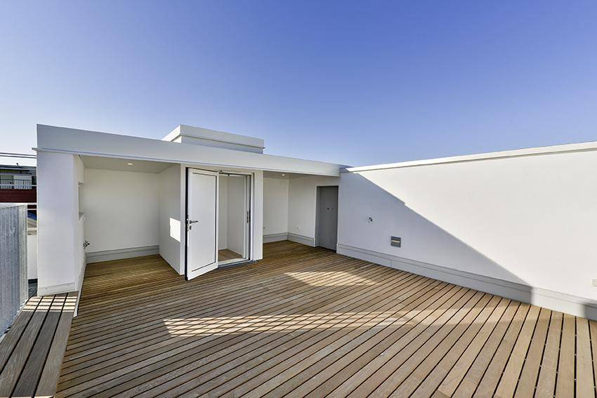 Geräumige Dachterrasse mit Holzdeck und direktem Aufzugzugang unter blauem Himmel.