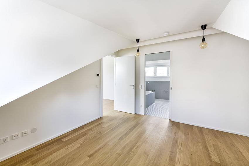 Dachgeschossraum mit Holzboden und Zugang zu einem modernen Badezimmer.