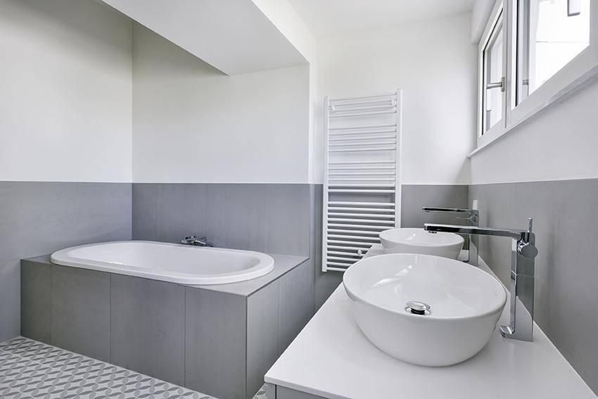 Elegantes Badezimmer mit Badewanne, Doppelwaschbecken, Handtuchheizkörper und Fenster.