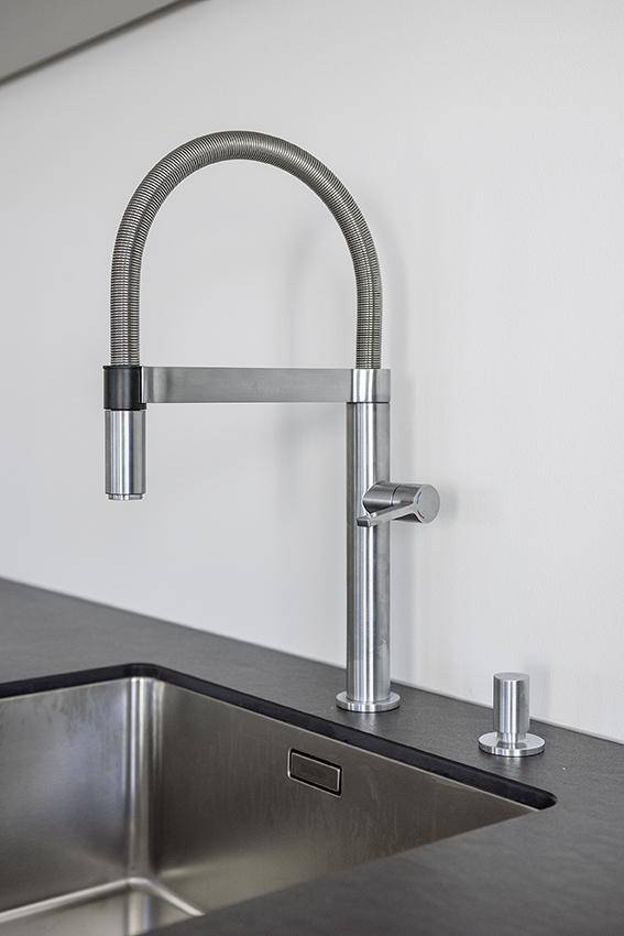 Moderne Küchenspüle aus Edelstahl mit flexiblem Wasserhahn und dunkler Arbeitsplatte.