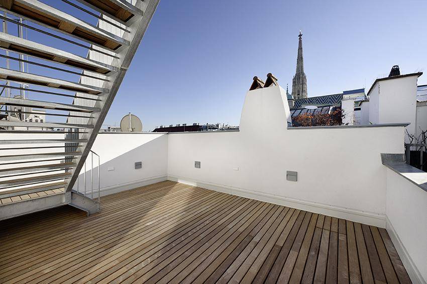 Leere Dachterrasse mit Holzdeck und Blick auf den Stephansdom, bereit zur Gestaltung.