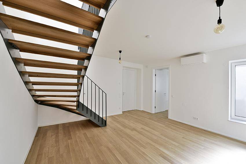 Heller Flur mit moderner Holztreppe und Klimaanlage, unmöbliert und geräumig.