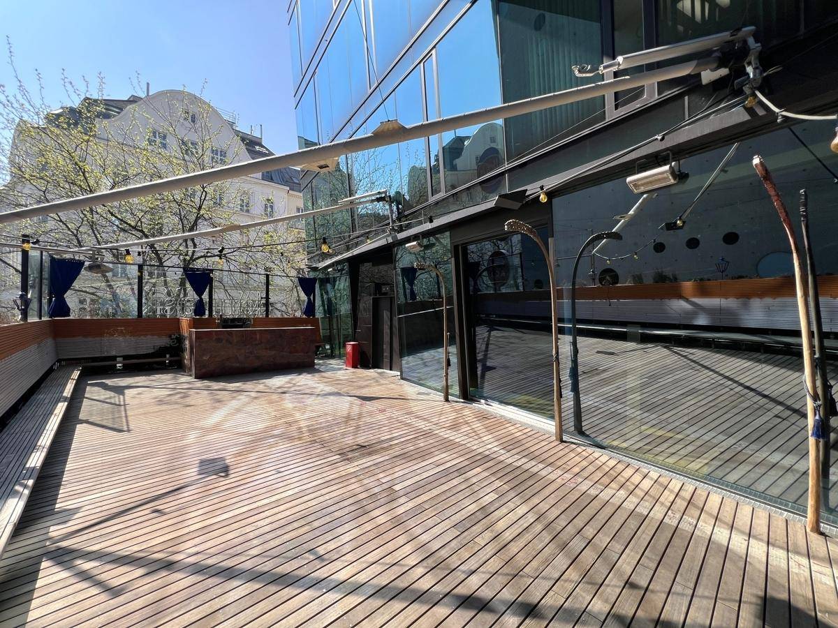 Eine weitläufige Holzterrasse mit Glasgeländer und ausfahrbarem Sonnenschutz, ideal für Veranstaltungen.