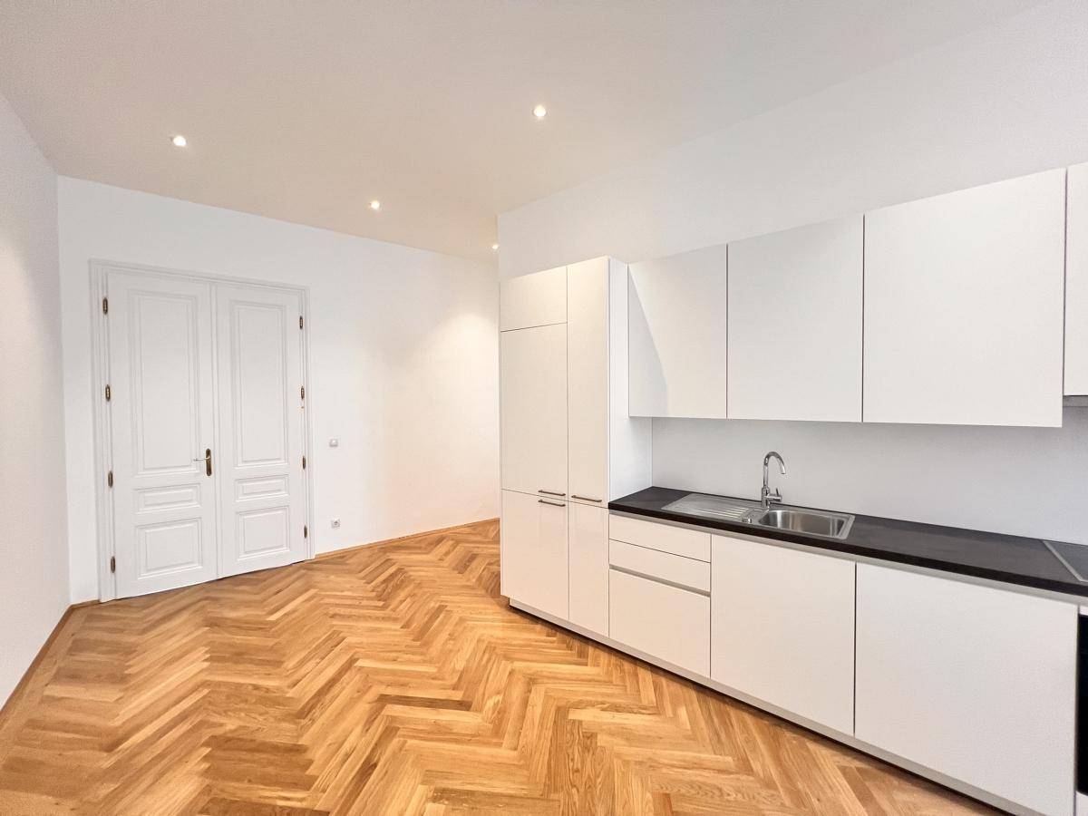 Neue Einbauküche mit weißen Schränken und dunkler Arbeitsplatte in einem Raum mit Fischgrätparkett.
