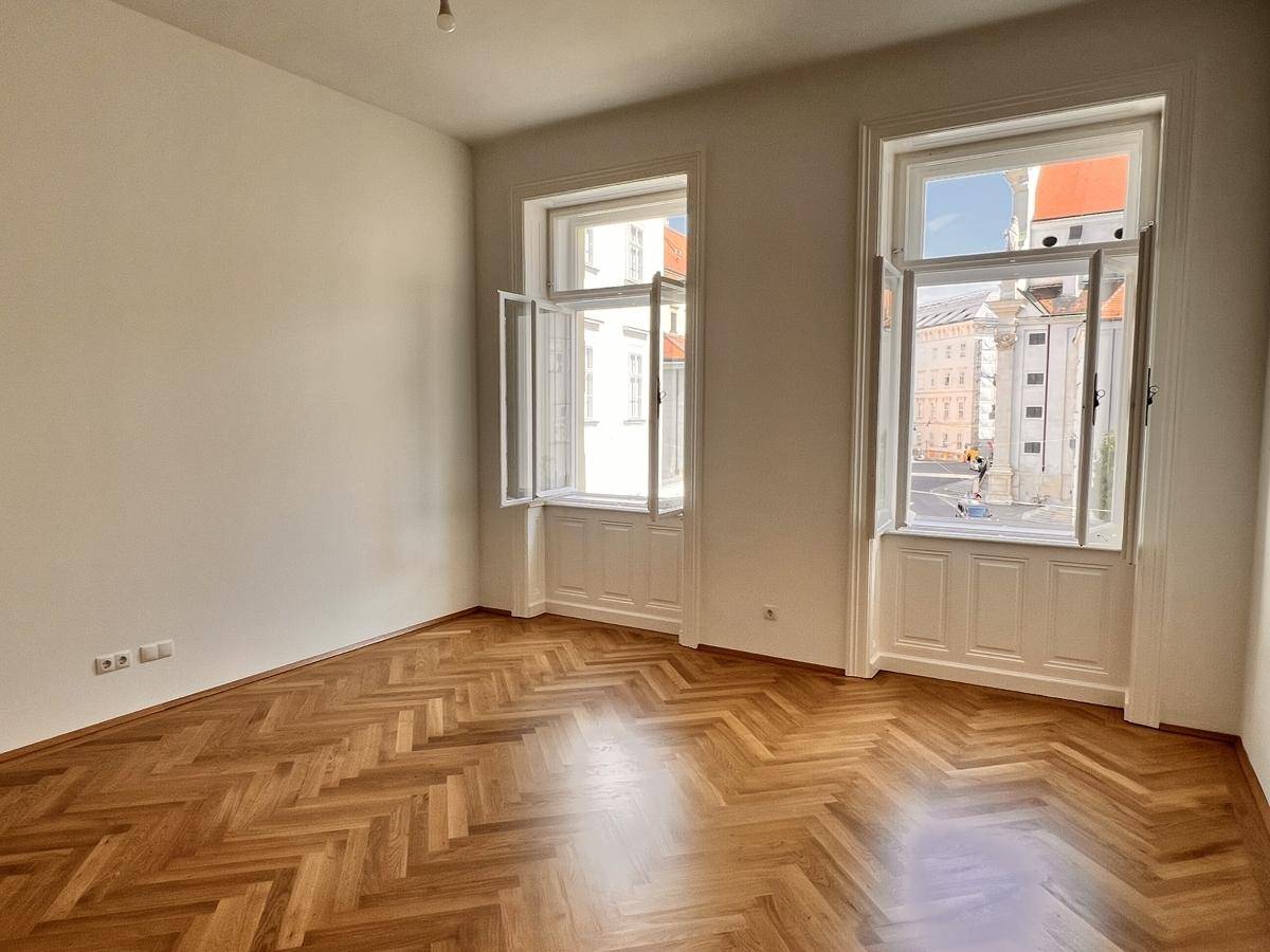 Geräumiger Raum mit Fischgrätparkett und geöffneten Fenstern, die einen Blick auf die Stadt bieten.