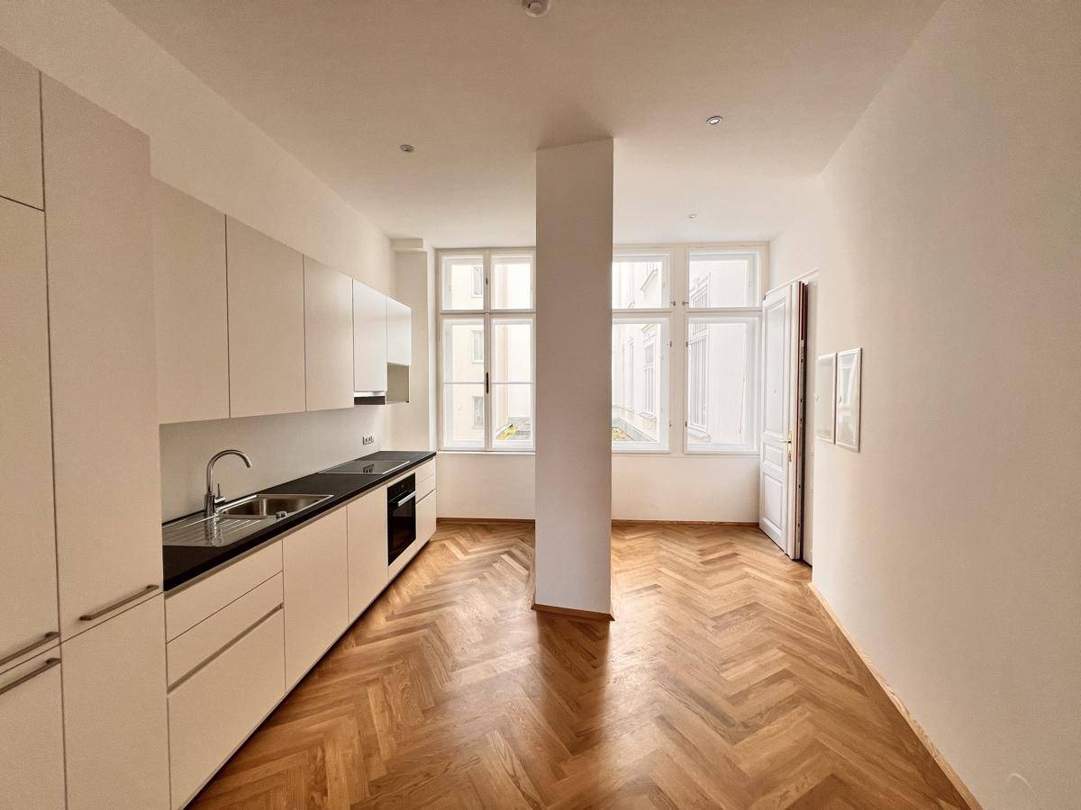 Helle Küche mit weißen Schränken, dunkler Arbeitsplatte und großen Fenstern mit viel Tageslicht.