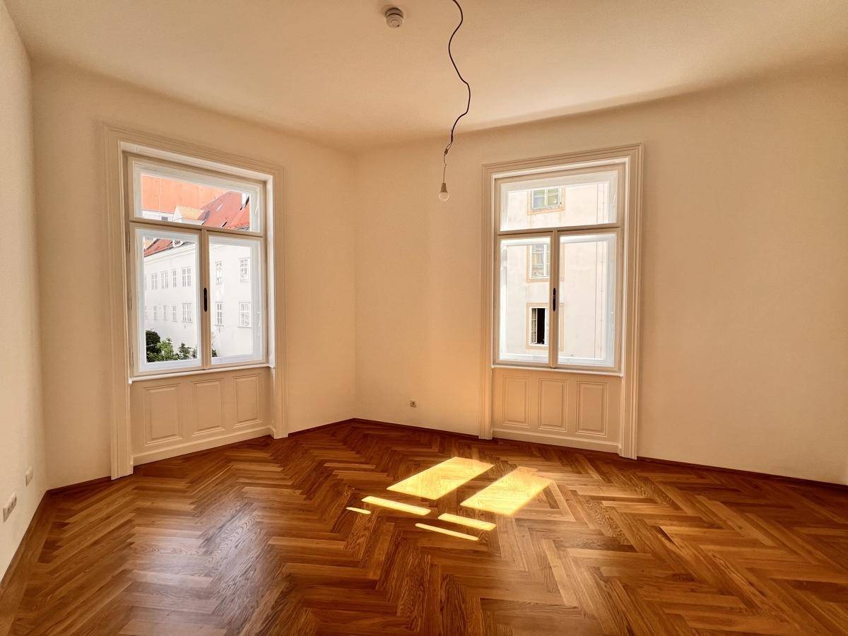 Sonniger Raum mit elegantem Fischgrätparkett und hohen Fenstern, die eine helle Atmosphäre schaffen.