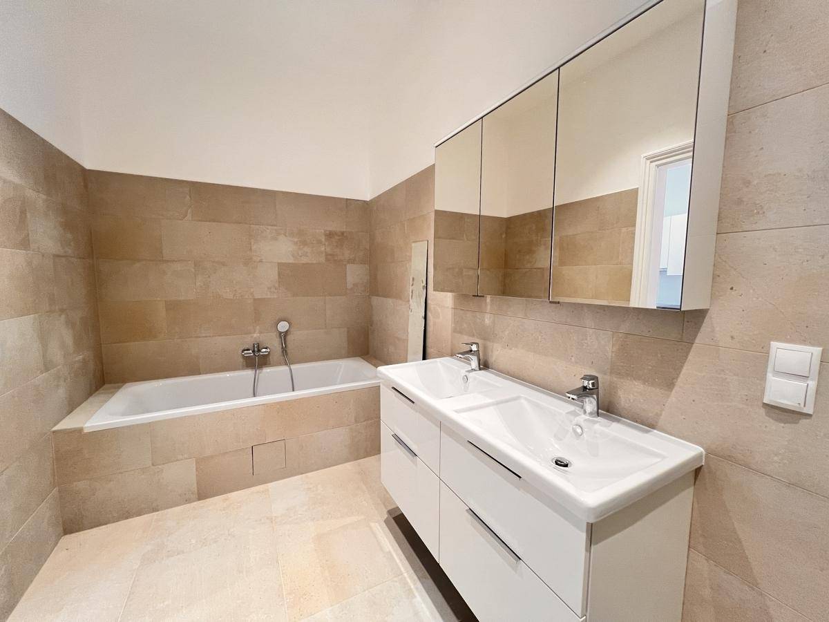 Modernes Badezimmer mit Doppelwaschbecken, integrierter Badewanne und beigefarbenen Fliesen.